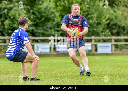 Älterer männlichen Spieler (Alter 30-50) bereitet die Kugel, da jüngere Spieler bereitet am Bewunderer Touch Rugby Festival in Lowestoft im Juli zu bewältigen Stockfoto