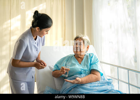 Asiatische Krankenschwester, Medikation und Glas Wasser zu älteren Frau im Krankenhaus. Medizin, Alter, Gesundheit und Personen Konzept Stockfoto