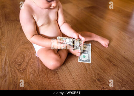 Baby spielt mit einigen Dollar, Rechnungen, die er auf dem Boden seines Hauses gefunden hat, Geld essen. Stockfoto