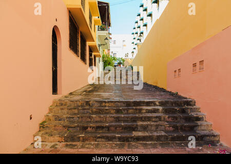 Ein altes Backsteingebäude, weg von einer ruhigen Gasse führt zu einer Straße durch den bunten Wohnhäuser in der Altstadt von San Juan, San Juan, Puerto Rico. Stockfoto