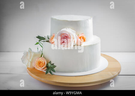 White Wedding zweistufigen Kuchen mit Blumen mit grünen Blättern in einem rustikalen Stil eingerichtet. Stockfoto