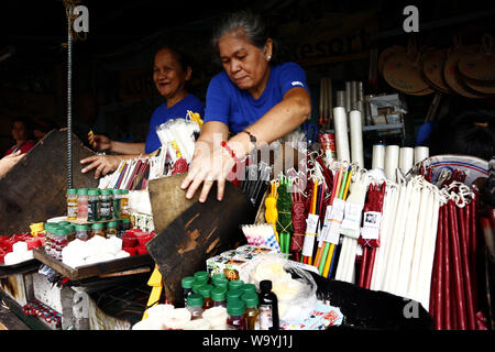 ANTIPOLO CITY, Philippinen - 12. AUGUST 2019: Kerze Hersteller sortiert farbige Gebet verkaufen Kerzen und pflanzliche Arzneimittel in einem Geschäft außerhalb einer Kirche. Stockfoto