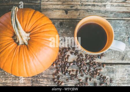 Nahaufnahme eines ganzen großen orangefarbenen Kürbisses mit Kaffee Bohnen und eine Tasse auf der Seite Stockfoto