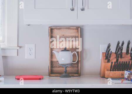 Weiße Teekanne auf einem Sockel in der Küche mit Küche Messer Sammlung auf der Seite Stockfoto