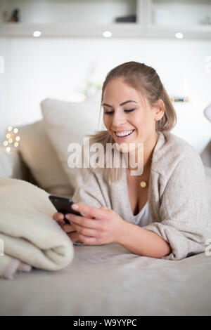 Schöne junge Dame ist mit einem Mobiltelefon, auf dem Sofa im Wohnzimmer zu Hause Stockfoto