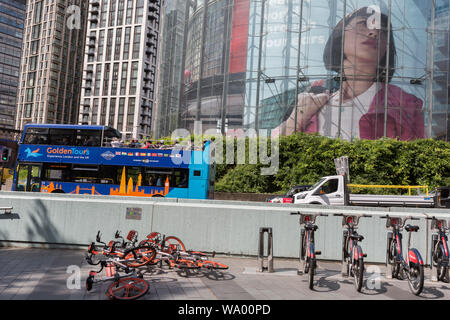 Mit einem Stapel der eingestürzten Mobikes auf dem Boden liegend, eine Tour-Bus wird in einem großen Bild einer Frau in einer Anzeige auf die zirkuläre Struktur des IMAX-Kino erscheint bei Waterloo, am 15. August 2019, in London, England. Stockfoto