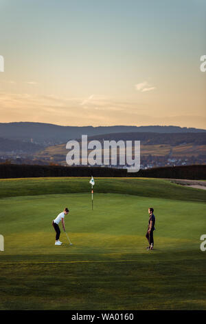 Junge Leute, beim Sonnenuntergang Golf in der schönen Landschaft auf Grün Stockfoto