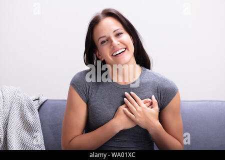 Glückliche junge Frau sitzt auf einem Sofa ihre Hand auf Herz halten Stockfoto