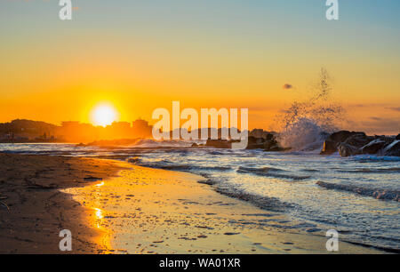 Sonnenuntergang am Meer im Sommer mit den Wellen auf die Felsen Stockfoto