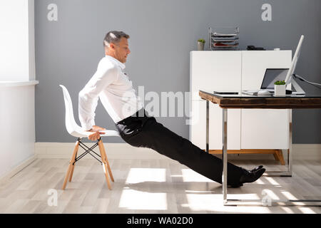 Seitenansicht eines Junge Unternehmer tun Trizeps Dips im Büro Stockfoto