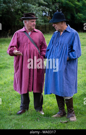 Zwei Männer in farbige Kittel als 19c Landarbeiter für eine BBC Countryfile Re-enactment gekleidet. Stockfoto