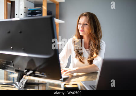 Lächelnden jungen Geschäftsfrau Arbeiten am Arbeitsplatz In die Vorderseite des Computers Stockfoto