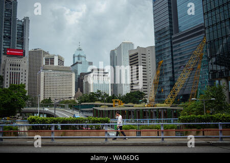 Hongkong, China. 16 Aug, 2019. Ein Passant überquert eine Brücke vor der Wolkenkratzer. In Hongkong gab es massive Proteste für mehr als zwei Monate. Die Demonstrationen wurden durch eine Gesetzesvorlage der Regierung ausgelöst - jetzt in der Warteschleife - Verdacht auf Auslieferung von Verbrechern zu China. Credit: Gregor Fischer/dpa/Alamy leben Nachrichten Stockfoto