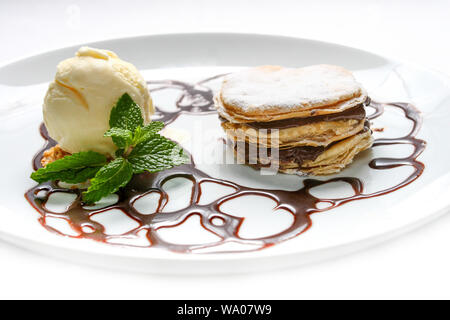 Französische Dessert millefeuille, mit Schokolade Sirup und Vanilleeis auf weißem Hintergrund. Mit Minze auf einem weißen Teller serviert. Stockfoto