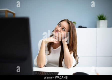 Lächelnden jungen Geschäftsfrau Tagträumen beim Sitzen in Ihrem Büro Schreibtisch Stockfoto