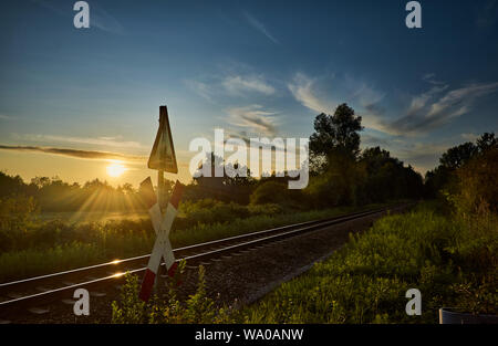 Schienen und ein Bahnübergang Zeichen vor der wunderschönen Natur und den Sonnenuntergang in Rastatt, Deutschland Stockfoto