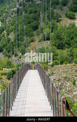 VAGLI SOTTO, Lucca, Italien August 8, 2019: Frau Kreuzung suspension Fußgängerbrücke über Vagli See in der Nähe von di Vagli Sotto Dorf. Stockfoto