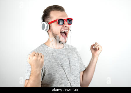 Jungen gutaussehenden Mann tragende rote Sonnenbrille gerne tanzen in Kopfhörer vorhören Seine bevorzugte Musik Hits auf isolierten weißen Hintergrund. Stockfoto