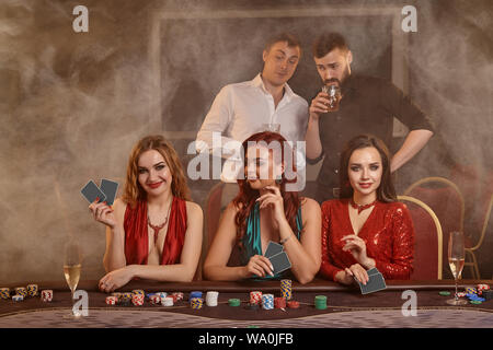 Konzentriert Begleiter sind Poker spielen im Casino. Goldene Jugend machen Wetten warten auf einen grossen Gewinn am Tisch gegen einen dunklen Rauch posing Stockfoto