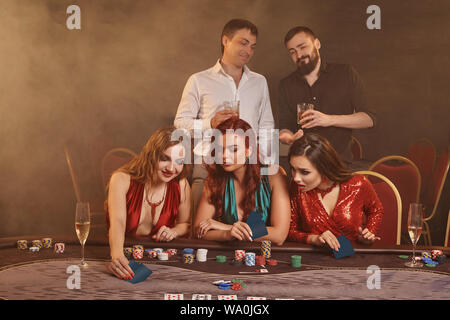 Konzentriert und Kollegen sind Poker spielen im Casino. Goldene Jugend machen Wetten warten auf einen grossen Gewinn am Tisch gegen einen dunklen Rauch posing Stockfoto