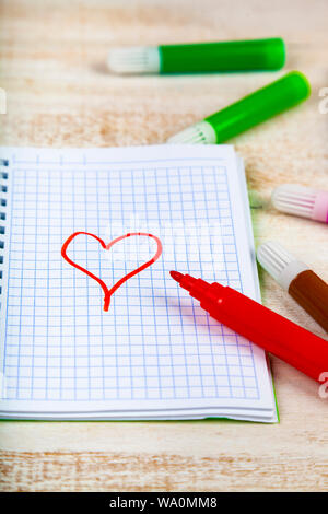 Filzstifte und Notebook. Rotes Herz ist auf einem karierten Blatt gezeichnet. Stockfoto