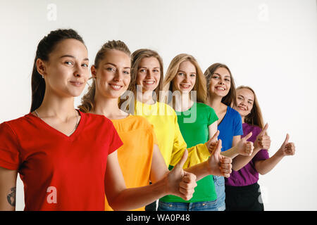 Junge Frauen getragen in LGBT Flagge Farben auf weißem Hintergrund. Kaukasische weibliche Modelle in hellen Hemden. Glücklich aus, Daumen nach oben. Vertrauen LGBT pride, Menschenrechte, Freiheit der Wahl Konzept. Stockfoto