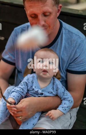 Prairieville, Michigan-ein-Jahr-alten Adam Hjermstad jr. hat sein Auge auf Marshmallows, dass sein Vater, Adam Hjermstad Sr., toasten Marshmallows über eine Stockfoto