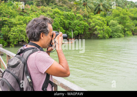 Ilha de Itamaraca, Brasilien - ca. August 2019: Mann auf einer Brücke ein Bild von den tropischen Regenwald und die Santa Cruz Kanal Stockfoto