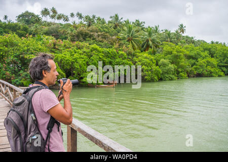 Ilha de Itamaraca, Brasilien - ca. August 2019: Mann auf einer Brücke ein Bild von den tropischen Regenwald und die Santa Cruz Kanal Stockfoto