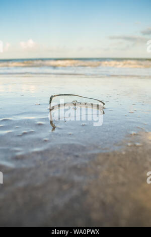 Gefährliches Stück Glasscherben auf dem Sand, das Meer im Hintergrund auf der Insel Itamaraca - Brasilien Stockfoto