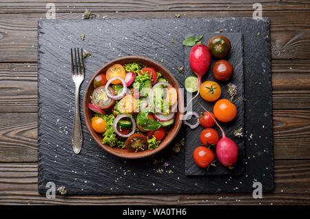 Draufsicht auf Salat von Kopfsalat, Tomaten, Radieschen, Gurken, Zwiebeln und Basilikum auf schiefer Fach Stockfoto