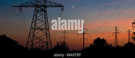 Elektrische Leitungen unter einem Nachthimmel mit Mond. Stromversorgung elektrische Leitung und Getriebe Turm Stockfoto