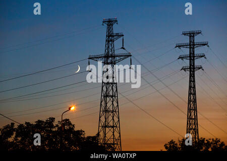 Elektrische Leitungen unter einem Nachthimmel mit Mond. Stromversorgung elektrische Leitung und Getriebe Turm Stockfoto