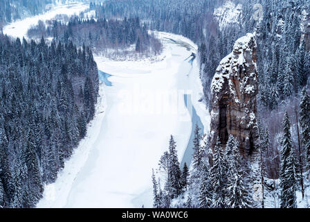 Blick von oben auf einem zugefrorenen Fluss in einer verschneiten bewaldeten felsigen Schlucht Stockfoto