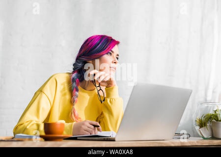 Mädchen mit bunten Haaren sitzen am Tisch und weg schauen nachdenklich Stockfoto