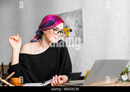 Mädchen mit bunten Haaren sitzt am Schreibtisch und Notizen in Wohnzimmer Stockfoto