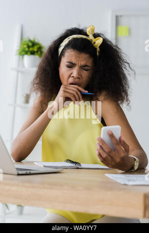 Selektiver Fokus der erschöpft afrikanische amerikanische Frau Gähnen und für Gesicht, während bei Smartphone suchen Stockfoto