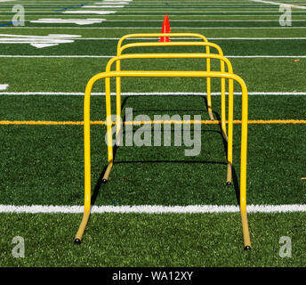 Eine Nahaufnahme von vier gelbe mini Hürden mit orange Kegel hinter Ihnen auf einem grünen Rasenfeld. Stockfoto