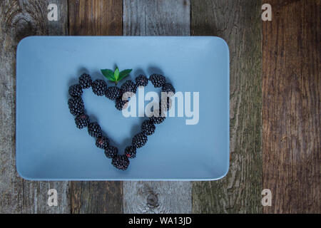 Herzform aus blackberry Beeren auf grauem Blech auf hölzernen Tisch Stockfoto