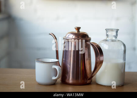 Nahaufnahme Kaffee Tasse, Kupfer Kaffeemaschine und eine Flasche mit Milch auf einem hellen Holz- Oberfläche, selektiver Fokus Stockfoto