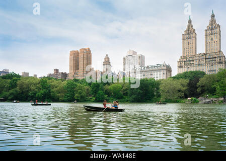 New York Central Park, Ansicht im Sommer von Menschen Ruderboote auf dem See mit West Central Park Gebäude im Hintergrund, Manhattan, NYC, USA Stockfoto