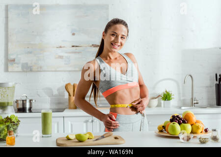 Glücklich und sportliche Frau mit Maßband und Messen Taille in der Nähe von Früchten Stockfoto