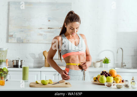 Junge Frau messen Taille in der Nähe von Früchten und Getränken Stockfoto