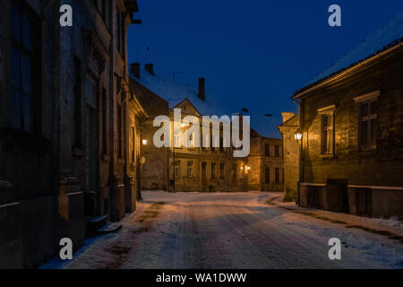 Schnee bedeckt Straße Kuldiga Altstadt während der Blauen Stunde durch eine Straße Lampen beleuchtet. Stockfoto