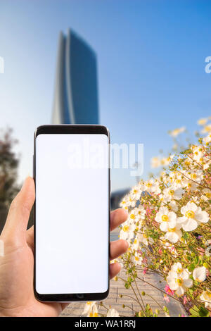 Hand mit modernen Smartphone mit Frühlingsblumen und verschwommenes moderne Gebäude, Büro Background, Business Konzept zu kopieren. Stockfoto