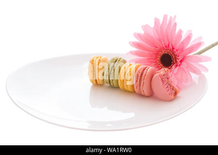 Französische süße Leckerei Makronen Vielzahl bunt und verschiedene süße Macarons auf weiße Platte mit rosa Blume auf weißem Hintergrund mit Stockfoto