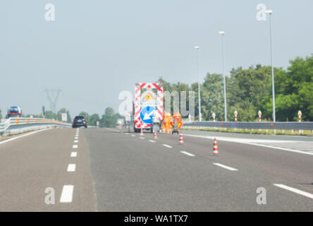 Verschwommenes Bild, Unterwegs arbeiten. Orange Kegel in der Mitte der Straße, Menschen, die an einer Straße. Stockfoto