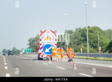 Verschwommenes Bild, Unterwegs arbeiten. Orange Kegel in der Mitte der Straße, Menschen, die an einer Straße. Stockfoto