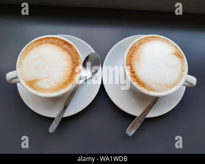 Lieben Kaffee Konzept, Ansicht von oben zwei weiße Tasse Cappuccino oder Kaffee Tasse Latte auf dunklen Tisch am Fenster mit Licht Schatten auf der Tischplatte im Cafe. Stockfoto