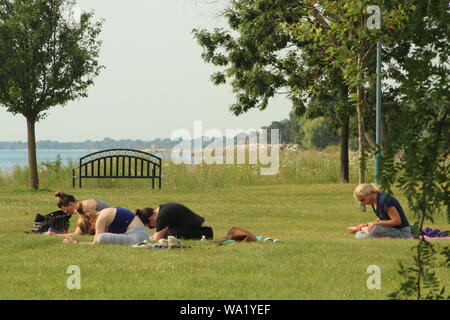 Drei Studenten und Ausbilder Üben Yoga außerhalb auf einem warmen August Morgen entlang des Lake Michigan Shoreline. Stockfoto